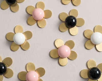 May include: Decorative flower-shaped objects with a brass-colored petal design. Each flower has a central sphere in black, white, or pink. The objects are arranged on a light gray surface.