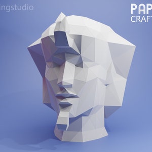 Op de afbeelding: Een wit papieren kunstwerk van een menselijk hoofd, met een geometrisch, polygoon ontwerp. Het beeld staat op een blauwe achtergrond. De tekst "PAPER CRAFT" is zichtbaar in de rechterbovenhoek van de afbeelding.