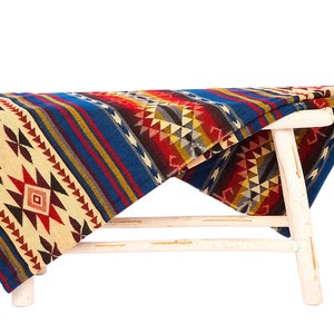 May include: A wooden stool with a colorful patterned blanket draped over it. The blanket features geometric designs in shades of red, blue, yellow, and white.