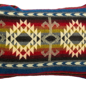 Puede incluir: Una almohada rectangular con un patrón geométrico de estilo suroeste en tonos de rojo, azul, blanco, negro y amarillo. La almohada está hecha de una tela suave y tejida.