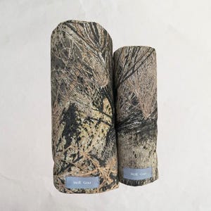 May include: Two fabric covered cylinders with a black, brown, and beige camouflage pattern. The cylinders have a label that reads "Moir. Goetz".