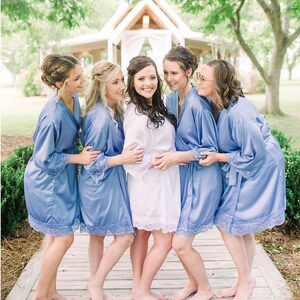 Könnte beinhalten: Fünf Frauen in blauen Satin-Roben mit Spitzenbesatz stehen auf einem Holzsteg. Sie lächeln und schauen in die Kamera. Die Braut steht in der Mitte und trägt eine weiße Satin-Robe mit Spitzenbesatz.