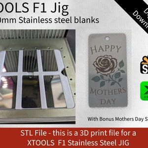 Könnte beinhalten: Ein 3D-gedruckter Jig zum Herstellen von Metalletiketten. Der Jig besteht aus weißem Kunststoff und hat vier Schlitze zum Halten von 20x50mm Edelstahlrohlingen. Das Bild zeigt auch ein Beispiel-Etikett mit dem Text "Happy Mothers Day" und einem Rosenmotiv.