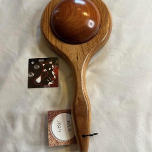 Puede incluir: Una herramienta de masaje de madera hecha a mano con una cabeza y un mango redondeados. La herramienta está hecha de una rica madera de color marrón rojizo. También hay una pequeña tarjeta con una ilustración de zorro y una etiqueta de precio.