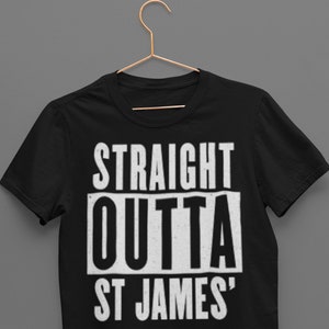 May include: Black t-shirt with the text "STRAIGHT OUTTA ST JAMES'" in a bold, white, distressed font. The shirt is hanging on a gold-colored hanger against a gray background. The t-shirt is a classic crew neck style.