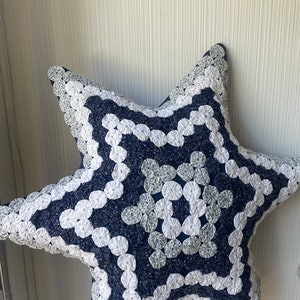 May include: A blue and white star-shaped pillow with a unique design made of fabric rosettes. The pillow is made of a soft, plush fabric and is perfect for adding a touch of whimsy to any room.