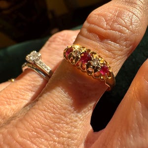 May include: A gold ring featuring a row of three round red rubies alternating with two clear white diamonds in a scalloped setting. The band is polished yellow gold, and the stones are set in a horizontal line across the top of the ring.