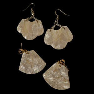 May include: Set of three white pearl earrings with gold accents. The earrings are shaped like a flower petal and have a shimmery finish.