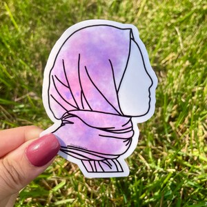 May include: A purple and pink watercolour sticker of a person wearing a headscarf. The sticker is outlined in black.