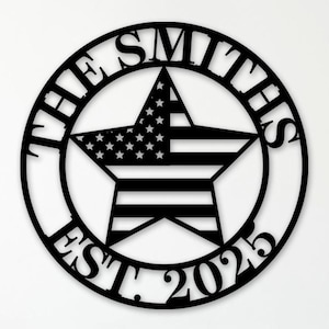 May include: Black metal wall art with a star design incorporating the American flag, set within a circle. The text reads "THE SMITHS" above and "EST. 2025" below. The artwork is displayed on a white wall.