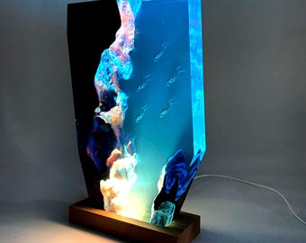 Könnte beinhalten: Dekorative Harzlampe mit Unterwassermotiv, die Taucher zeigt. Die Lampe hat einen Holzsockel und eine rechteckige Form mit einem schwarzen, blauen und weißen Design. Die Lampe wird mit einem weichen, warmen Licht beleuchtet.
