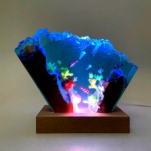 May include: A decorative resin aquarium scene with colorful fish, coral, and jellyfish, illuminated by blue and red LED lights. The artwork is set on a wooden base, creating a captivating underwater diorama.