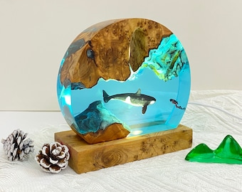 May include: A wooden base with a round, clear resin orb containing a black and white orca figurine and blue and green resin accents. The orb is lit from within.