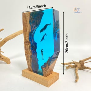 May include: A blue resin sculpture of a diver and two whales, set in a wooden base. The sculpture is 13 inches wide and 8 inches tall.