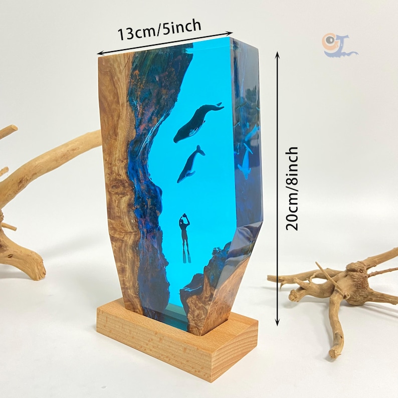 May include: A blue resin sculpture of a diver and two whales, set in a wooden base. The sculpture is 13 inches wide and 8 inches tall.