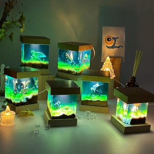 Puede incluir: Seis pequeñas lámparas de noche en forma de cubo de madera con inserciones de resina transparente. Cada cubo presenta una figura de dragón en miniatura diferente en el interior. La resina se ilumina con un brillo verde.