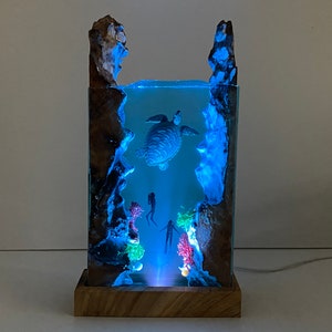 May include: A resin sculpture depicting an underwater scene with a sea turtle, coral, and divers. The sculpture is illuminated with blue LED lights and sits on a wooden base.