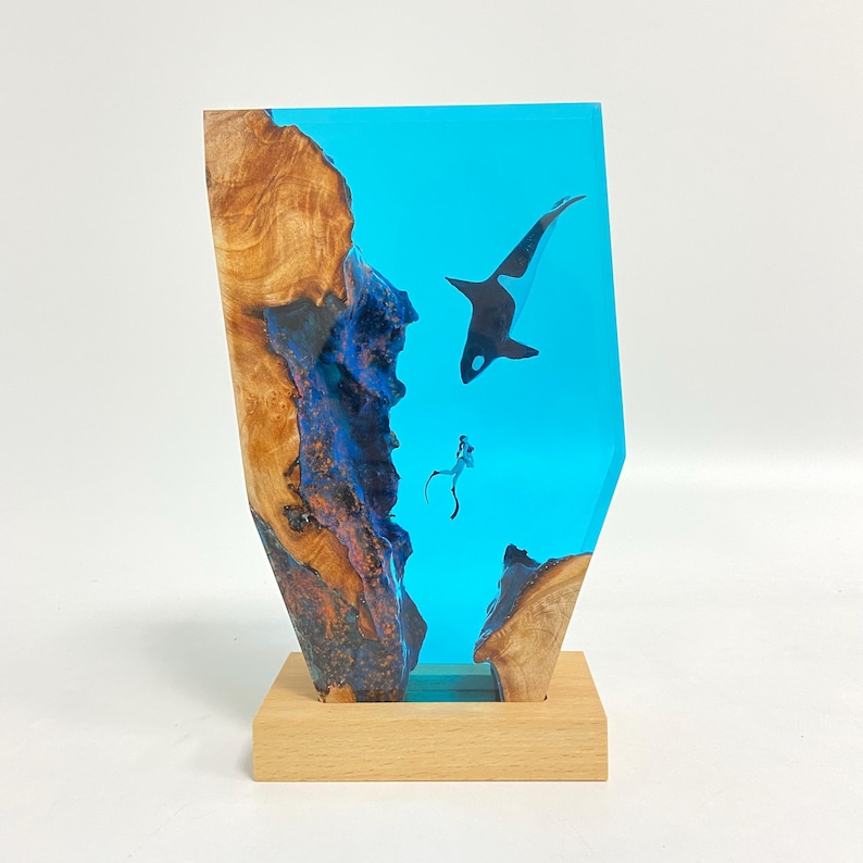 May include: A blue resin sculpture of a killer whale and a diver, set in a wooden base. The resin is clear and shows the wood grain underneath.