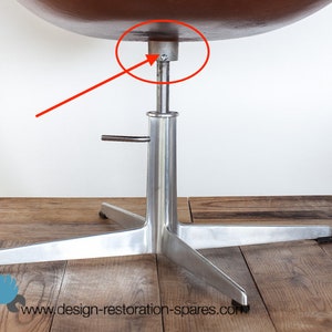 Könnte beinhalten: Ein Stuhl im Mid-Century-Modern-Stil mit einem braunen, abgerundeten Sitz und einem polierten Metallsockel. Der Sockel hat ein Vier-Sterne-Design. Die Höhe des Stuhls ist verstellbar. Der Stuhl steht auf einem Holzboden.