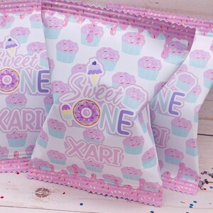 May include: Pink and white treat bags with a cupcake pattern and the text "Sweet One Xari".