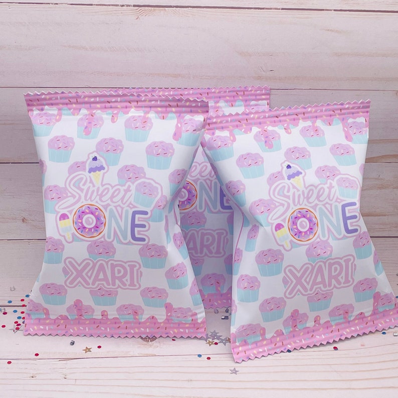 May include: Three pink and white treat bags with a cupcake pattern. The bags have the text "Sweet One" and a name on them.