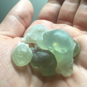 May include: A collection of smooth, sea glass pieces in shades of green. The glass is translucent and has a slightly frosted appearance.