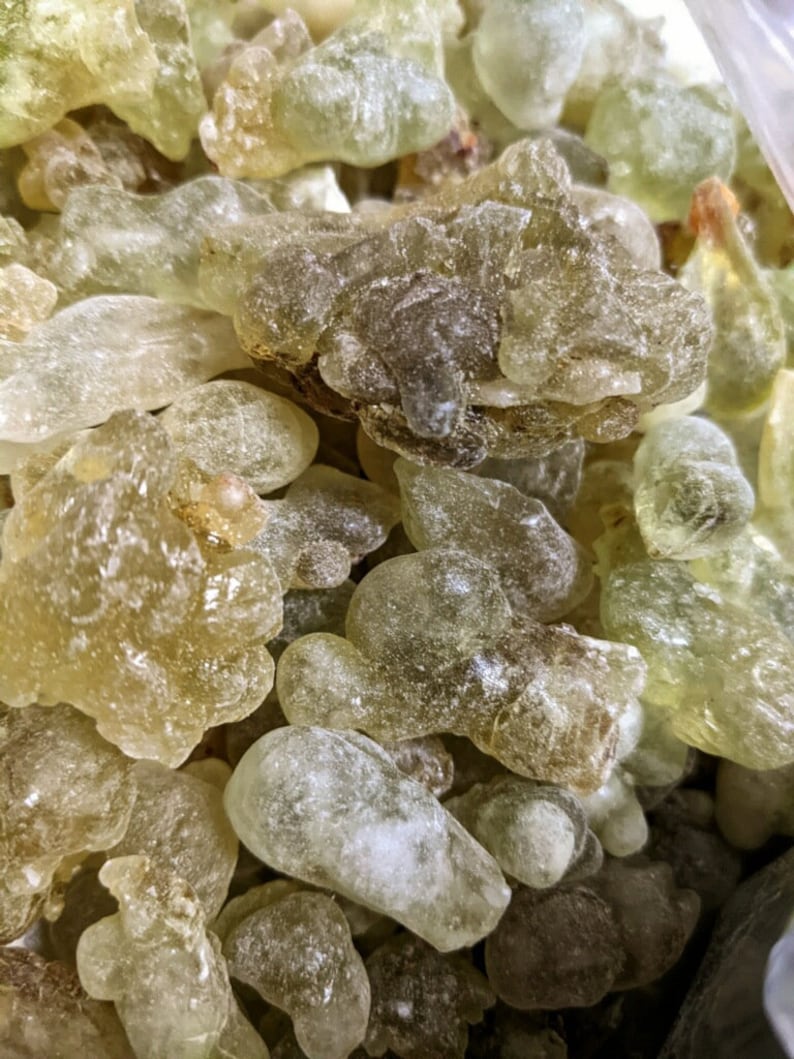 May include: Close-up of a pile of translucent, light green and brown resin pieces. The resin is irregularly shaped and has a slightly rough texture.