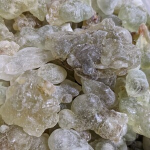 May include: A close-up of a pile of translucent, light green and white resin pieces. The resin pieces are irregularly shaped and have a slightly frosted appearance.