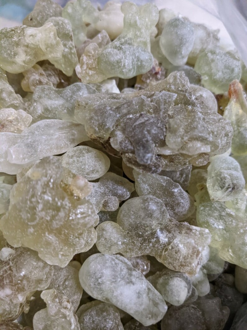 May include: A close-up of a pile of translucent, light green and white resin pieces. The resin pieces are irregularly shaped and have a slightly frosted appearance.