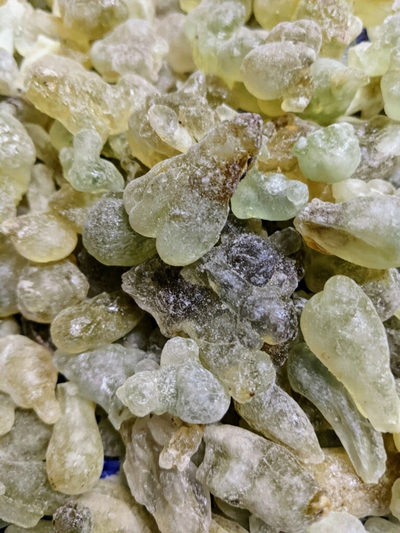 May include: A close-up of a pile of translucent green and brown resin pieces. The resin is irregularly shaped and has a rough, textured surface.