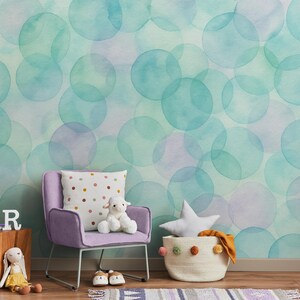 May include: A wallpaper featuring a watercolor pattern of overlapping teal and light purple circles. The room includes a light purple armchair, a white pillow with colorful dots, a plush lamb, a star-shaped pillow, and a woven basket.