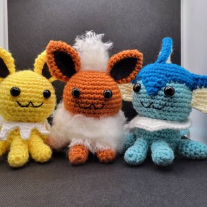 Puede incluir: Tres peluches de crochet que representan a los personajes de Pokémon Eevee, Flareon y Vaporeon. Eevee es de color marrón claro con pelaje blanco, Flareon es naranja con pelaje blanco y Vaporeon es azul claro con pelaje blanco.