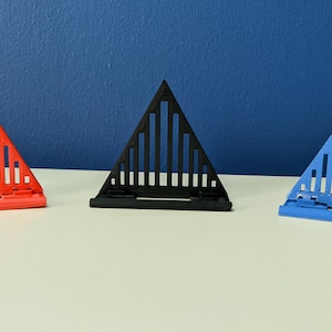 May include: Three triangular phone stands in red, black, and blue. Each stand has a geometric design with vertical lines.