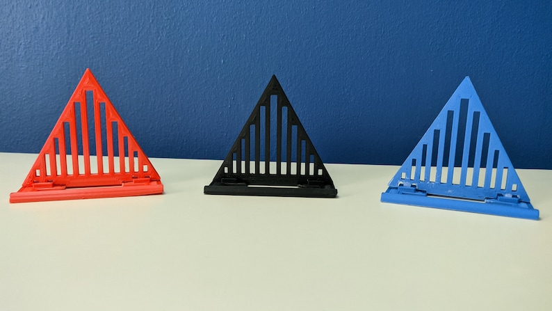 May include: Three triangular phone stands in red, black, and blue. Each stand has a geometric design with vertical lines.