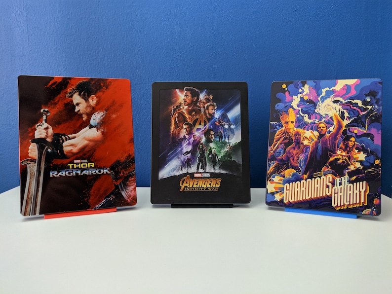 May include: Three Marvel movie Blu-ray cases with colorful artwork. The left case features Thor Ragnarok with Thor holding a sword. The middle case features Avengers Infinity War with a group of superheroes. The right case features Guardians of the Galaxy with a group of characters in a colorful nebula.