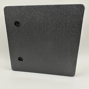 May include: A black, textured, rectangular panel with rounded corners. Two circular holes are visible near the top and bottom. The panel has a slightly angled shape, and the surface has a subtle, granular texture.