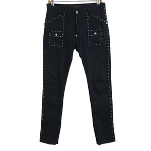 May include: Black skinny jeans with silver studs along the sides and pockets. The jeans have a zipper fly and button closure.