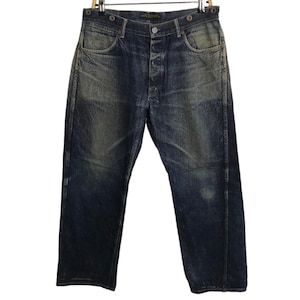 May include: Dark wash denim jeans with a button fly and faded areas. The jeans are hanging from a metal hanger. The denim has a worn appearance, with lighter patches and subtle distressing. The jeans have a classic five-pocket design.