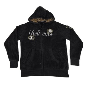 May include: Black zip-up hoodie with a soft, textured fabric. The hood lining features a leopard print. The word "Believers" is embroidered across the chest in silver script. Patches with skull and monkey designs are on the front and sleeve.