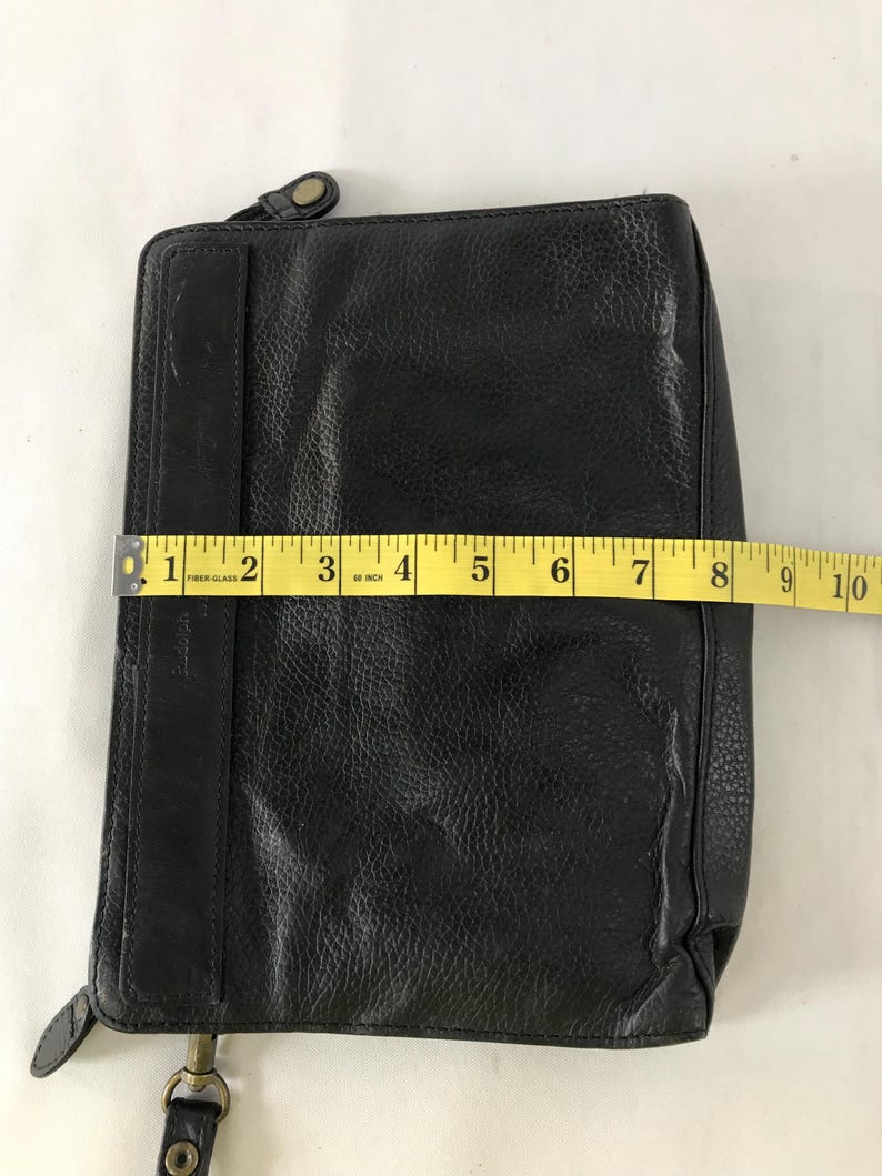 May include: Black leather wallet with a textured surface. The wallet is rectangular and measures approximately 23 cm in length. It features a zipper closure and a strap with a metal clasp.