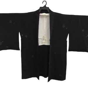 May include: Black kimono with white lining and a cream-coloured tie closure. The kimono has a long, open design with wide sleeves and is hanging on a black hanger. There are several dark spots on the black fabric.