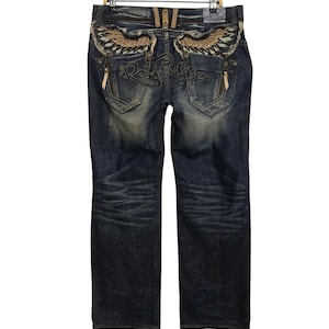 Op de afbeelding: Blauwe denim jeans met een distressed look en geborduurde vleugels en de tekst "Red Pepper" op de achterzakken.