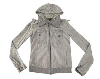 Könnte beinhalten: Hellgraue Kapuzenjacke mit durchgehendem Reißverschluss. Die Jacke hat zwei Vordertaschen mit Reißverschlüssen und graue Ärmel. Die Kapuze hat einen Kordelzug. Die Jacke ist aus weichem Material.