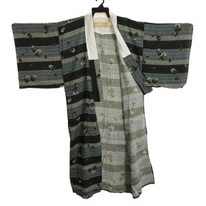 May include: A vintage kimono with a black, gray, and white striped pattern. The kimono features a white collar and is decorated with a repeating pattern of abstract shapes. The sleeves are wide and the garment is open in the front.