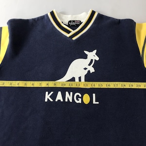 May include: Navy blue Kangol V-neck sweatshirt with yellow sleeves and black stripes. Features a white kangaroo logo and the brand name in white. The collar has white, black, and yellow trim. The sweatshirt measures approximately 24 inches across.