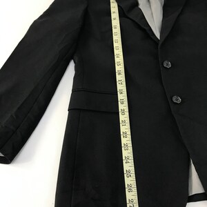 Puede incluir: Blazer negro con cierre de tres botones, solapa de muesca y forro interior gris. Una cinta m&eacute;trica muestra que el blazer mide aproximadamente 74 cm de largo. El blazer tiene un dise&ntilde;o cl&aacute;sico y entallado.