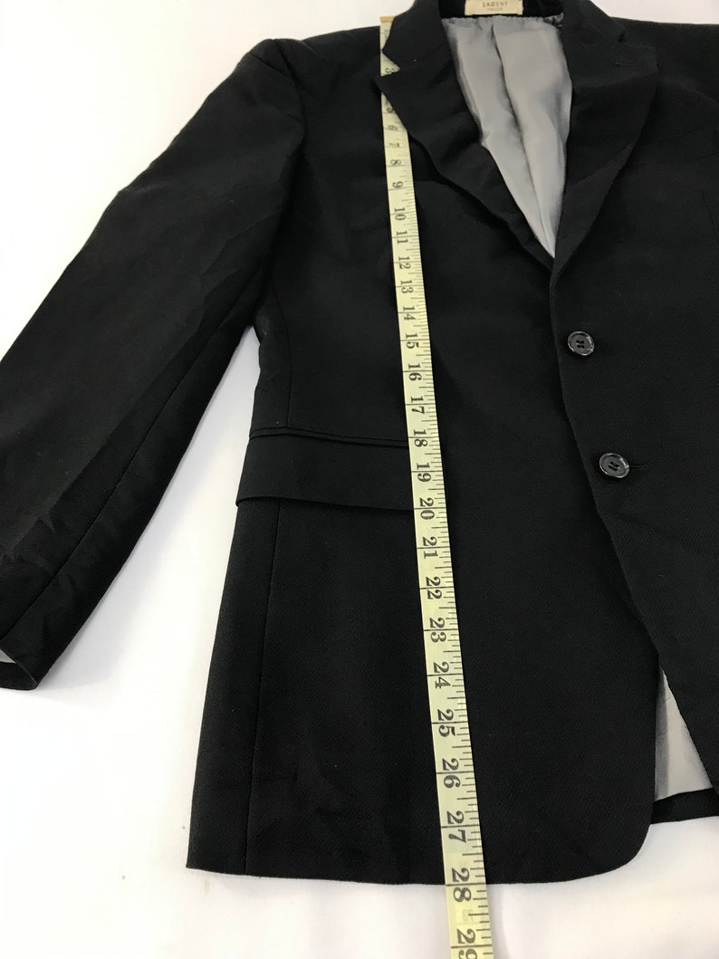 Puede incluir: Blazer negro con cierre de tres botones, solapa de muesca y forro interior gris. Una cinta m&eacute;trica muestra que el blazer mide aproximadamente 74 cm de largo. El blazer tiene un dise&ntilde;o cl&aacute;sico y entallado.