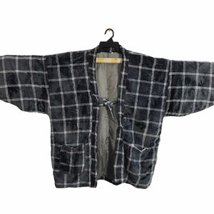 May include: A black and white plaid kimono-style jacket with long sleeves and two front pockets. The jacket is made of a soft, textured fabric and features a tie closure at the waist. The interior lining is a solid gray color.
