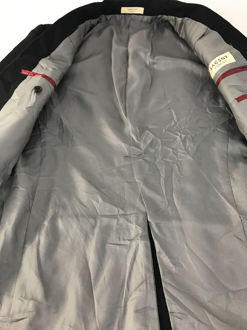 Puede incluir: Blazer negro con forro de sat&eacute;n gris. El interior presenta una etiqueta que dice "SACSNY YSACS". El blazer tiene un cierre de un solo bot&oacute;n y costuras rojas.