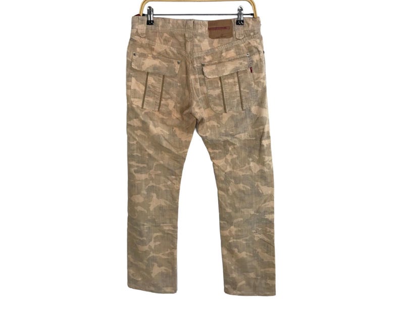 May include: Beige camouflage print pants with a brown leather patch on the back.